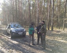 Widok strażników łowieckich udzielających wywiadu  na tle  pojazdu służbowego oraz lasu